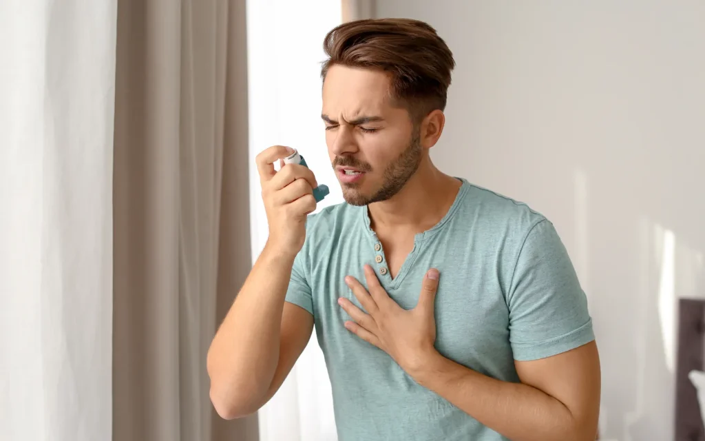 A man with an asthma inhaler while he struggles to breathe due to poor indoor air quality