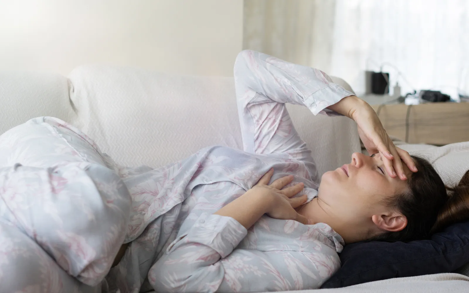 A woman lying down on her bed holding her head, representing chronic fatigue and migraines caused by mold exposure