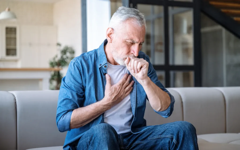 A man coughing and holding his chest due to respiratory problems caused by mold exposure in his home