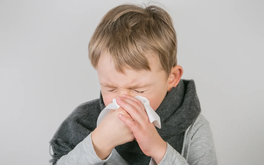 A young child sneezing into a tissue, representing a common mold exposure symptom
